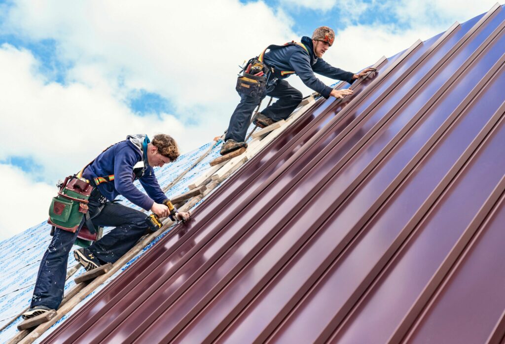 Roofers installing metal roof under blue sky.